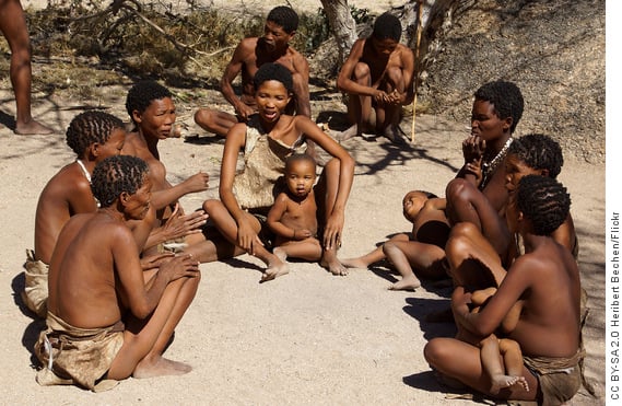 Bushman group of men, women and children sitting on sand in a cirlce