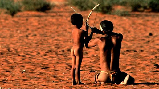 Bushman in desert teaching child how to use bow and arrow