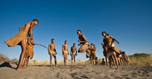 Group of bushmen skipping happily in sand with big blue sky