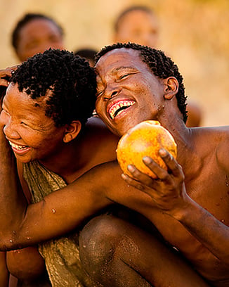 A Kalahari bushmen laughing with joy holding a melon and embracing another happy smiling Bushman