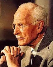 Carl Jung as an older man sits with his hand clasped in front of him