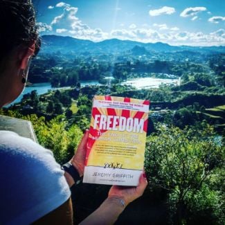 FREEDOM book held by girl in front of Colombian lake - World Transformation Movement Commendations