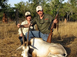 Elated hunter posing with his trophy kill of an Oryx and rifle in hand