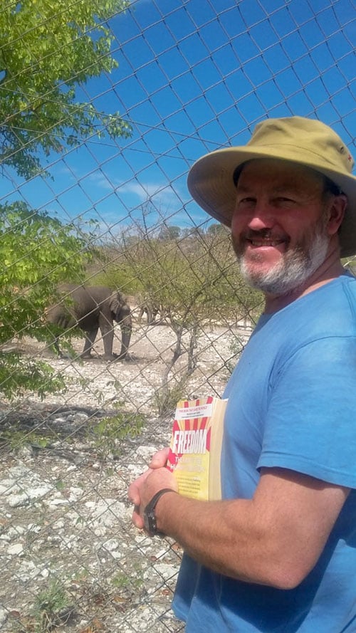 James Moffett holding the book FREEDOM with an elephant in the background