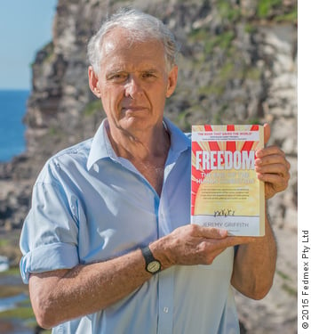 Portrait photograph of Jeremy Griffith holding his book ‘FREEDOM’ on a headland