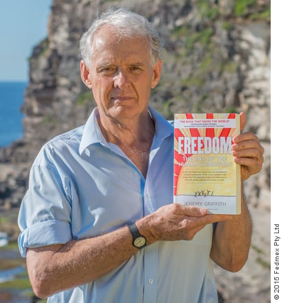 Portrait photograph of Jeremy Griffith holding his book ‘FREEDOM’ on a headland