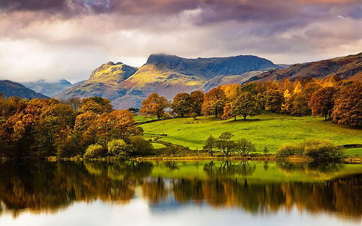 Painting of a beautiful view across a still lake reflecting the lush green hills behind in the Lakes District, England