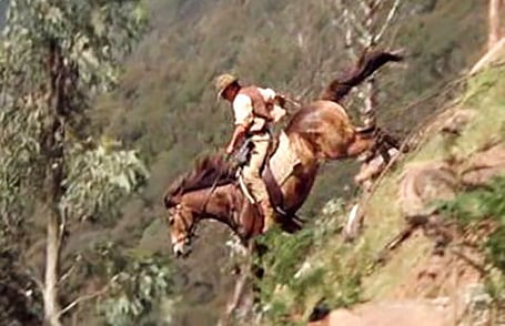 A stockman riding a horse at speed down a steep and rugged slope in the Australian bush