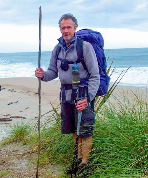 Founder of the World Transformation Movement NZ Centre, Pete Sadler standing on a beach