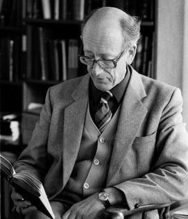 Photograph of Professor John Morton seated reading a book