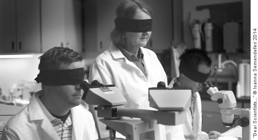 Scientists wearing blindfolds while looking into microscopes in a laboratory