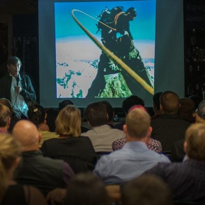 Tim Macartney-Snape talking to an audience with a background slide image from his climbing expedition
