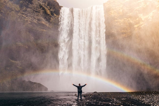 Man under rainbow in front of waterfall