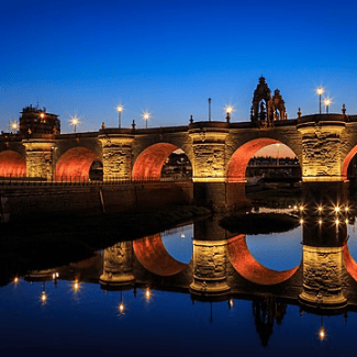 Arched bridge and lights reflected over still water