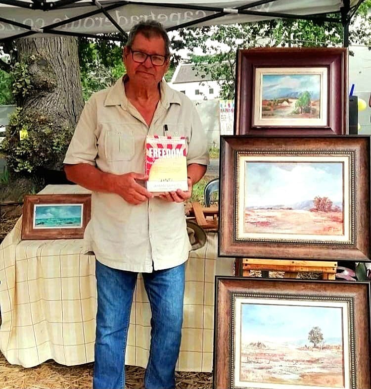 John Mulder holding FREEDOM standing next to some of his landscape paintings