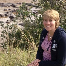 Photograph of Yvonne Hayes in front of a waterhole with lots of hippos in Kenya